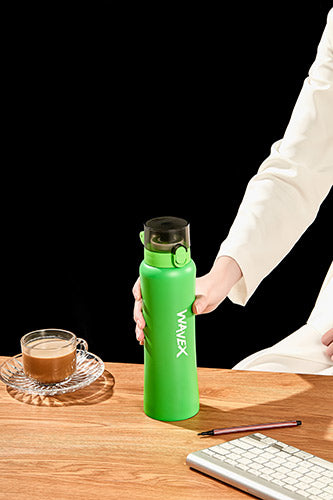 A person seated at a desk with a stainless steel 550ml green water bottle beside them.