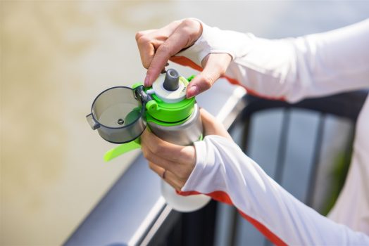 A woman holds a water bottle with a green lid, promoting healthy hydration and wellness.