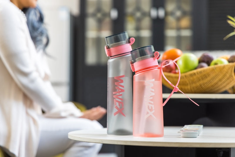 Two water bottles placed on a table beside a woman, highlighting hydration in a casual setting